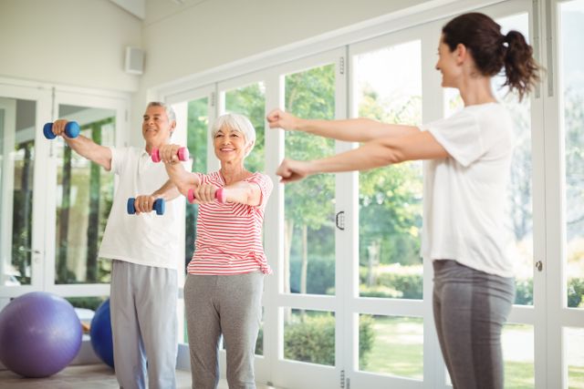 Female trainer assisting senior couple in performing exercise - Download Free Stock Photos Pikwizard.com