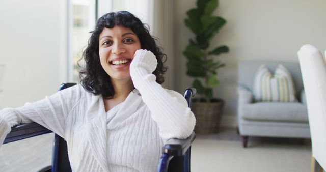 Portrait of happy biracial disabled woman in wheelchair laughing in living room. wellbeing and domestic lifestyle with physical disability.