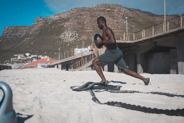 African american man exercising with weights and rope on beach on sunny day - Download Free Stock Photos Pikwizard.com