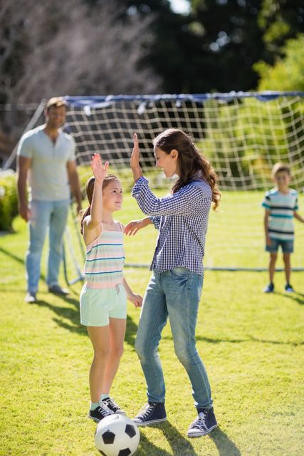 Mother and daughter giving high five while playing football in park - Download Free Stock Photos Pikwizard.com