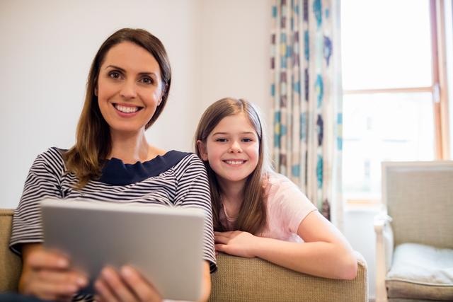 Mother and daughter sitting on sofa using digital tablet in living room at home