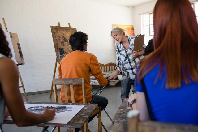 Female teacher examining students painting at table in art class