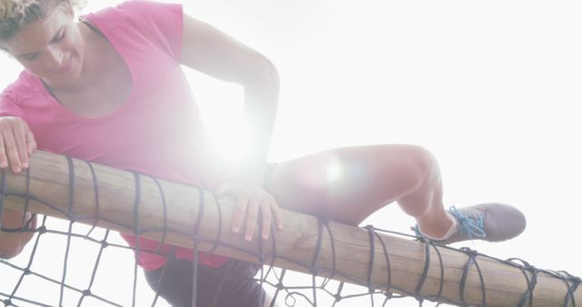 Happy caucasian female woman in pink t shirts climbing over nets on climbing frame at bootcamp. Female fitness, challenge and healthy lifestyle.