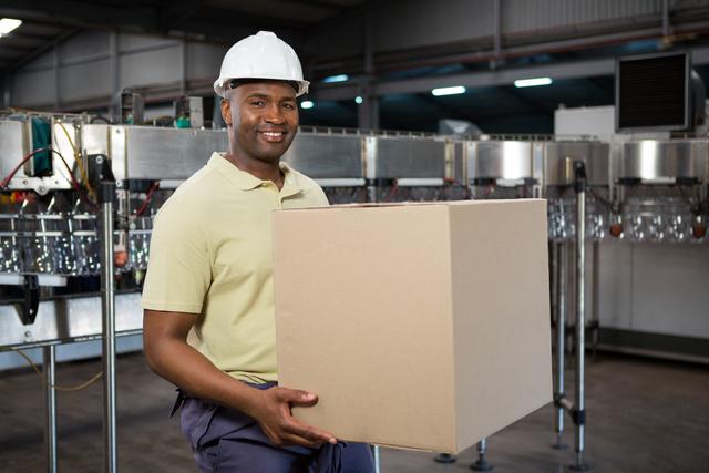 Smiling male employee carrying cardboard box in juice factory - Download Free Stock Photos Pikwizard.com