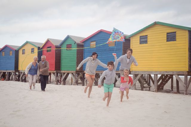 Happy multi-generation family running by beach huts at beach - Download Free Stock Photos Pikwizard.com