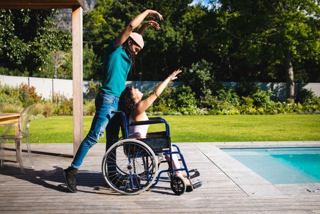 Side view of young multiracial man dancing with disabled woman on wheelchair at poolside - Download Free Stock Photos Pikwizard.com