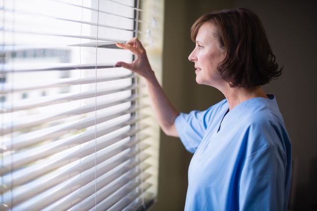 Thoughtful nurse looking out through window - Download Free Stock Photos Pikwizard.com