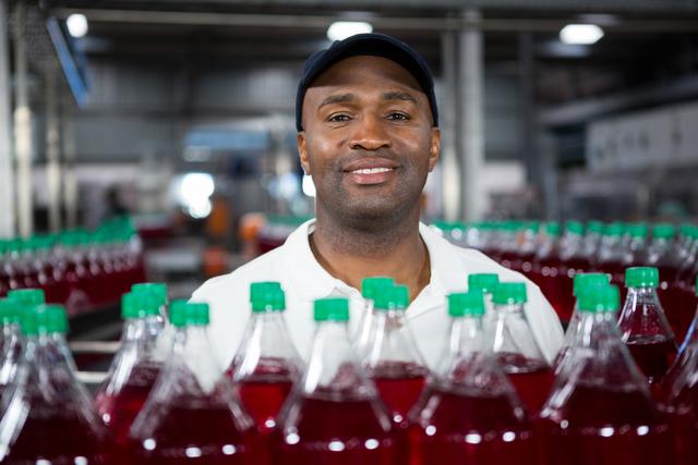 Close up portrait of smiling male employee standing by juice bottles in factory