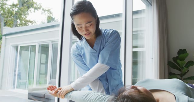 Smiling asian female physiotherapist treating arm of female patient lying on bed at surgery. physiotherapy, health and healthcare services.