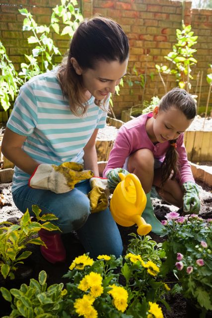Smiling mother kneeling by girl watering plants - Download Free Stock Photos Pikwizard.com