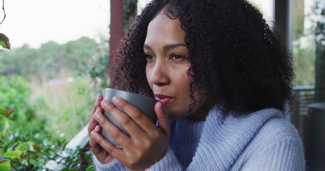 Happy mixed race woman enjoying drinking coffee standing on balcony in countryside. spending free time at home.
