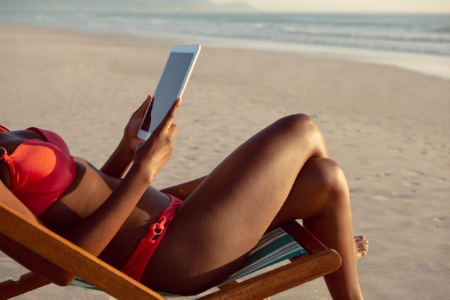 Low section of woman using digital tablet while relaxing in a beach chair on the beach
