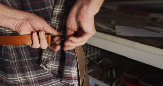 Close up of hands of caucasian male knife maker in workshop tying apron. independent small business craftsman at work.