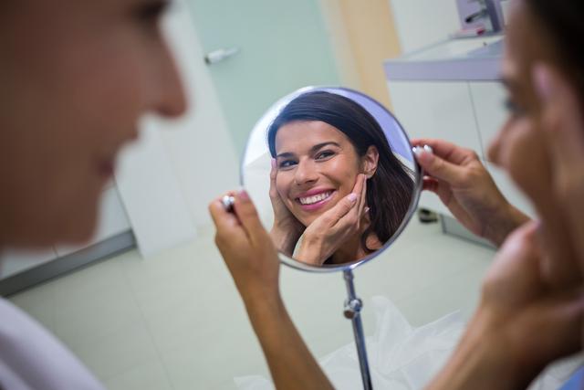 Woman checking her skin in the mirror after receiving cosmetic treatment - Download Free Stock Photos Pikwizard.com