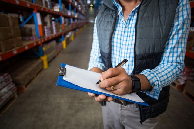Mid section of warehouse worker writing on clipboard - Download Free Stock Photos Pikwizard.com