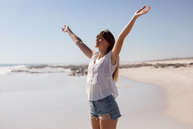 Beautiful woman with arms stretched out standing on beach in the sunshine - Download Free Stock Photos Pikwizard.com