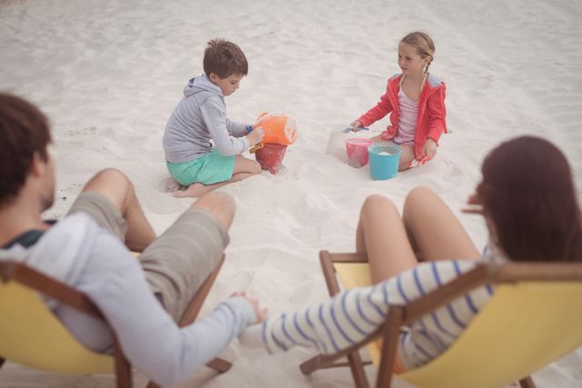Siblings playing by parents relaxing on launge chairs at beach - Download Free Stock Photos Pikwizard.com