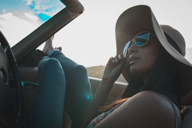 Mixed race woman wearing sun glasses looking sitting in convertible car. summer holiday road trip on a country highway by the coast.