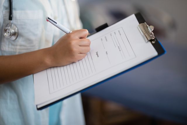 Midsection of female doctor writing on clipboard - Download Free Stock Photos Pikwizard.com