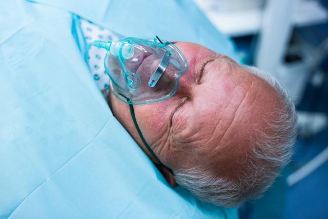 Patient lying on bed with oxygen mask in operation room at hospital