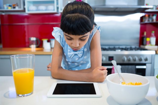 Girl looking at tablet computer while sitting with breakfast - Download Free Stock Photos Pikwizard.com