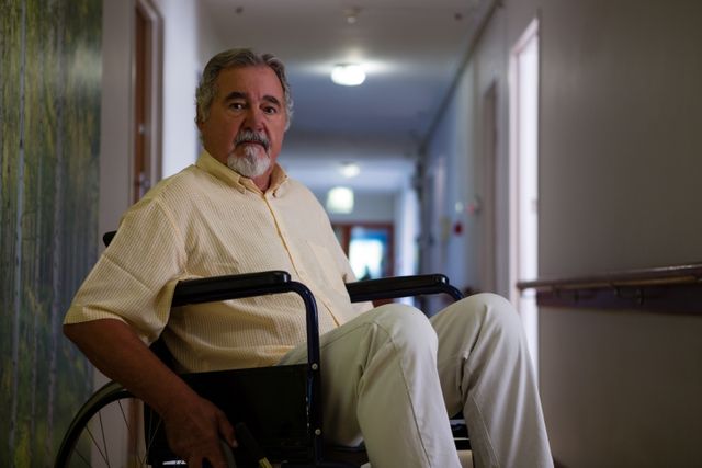 Portrait of senior man sitting on wheelchair in corridor - Download Free Stock Photos Pikwizard.com