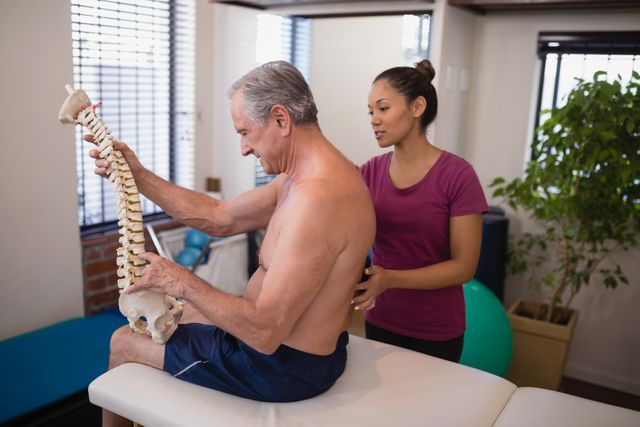 Shirtless male patient holding artificial spine while female therapist examining back - Download Free Stock Photos Pikwizard.com