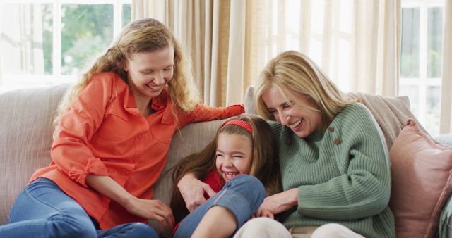Image of happy caucasian mother and grandmother tickling laughing granddaughter on couch. Family, domestic life and togetherness concept digitally generated image.