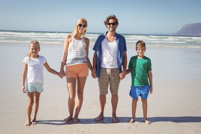Portrait of happy family holding hands while standing together at beach during sunny day