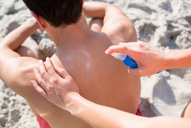 Woman applying spray on man back at beach - Download Free Stock Photos Pikwizard.com