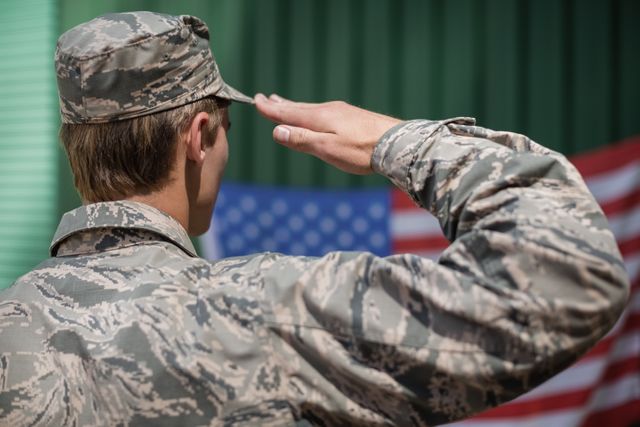 Rear view of military soldier giving salute to american flag in boot camp
