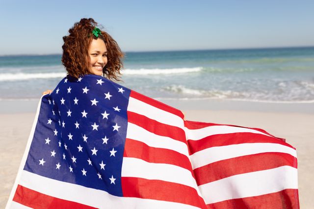 Beautiful young woman wrapped in american flag looking at camera on beach in the sunshine - Download Free Stock Photos Pikwizard.com