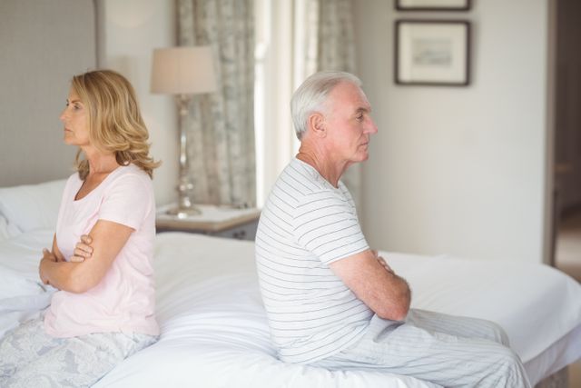 Upset senior couple sitting back to back on bed- Download Free Stock Photos Pikwizard.com