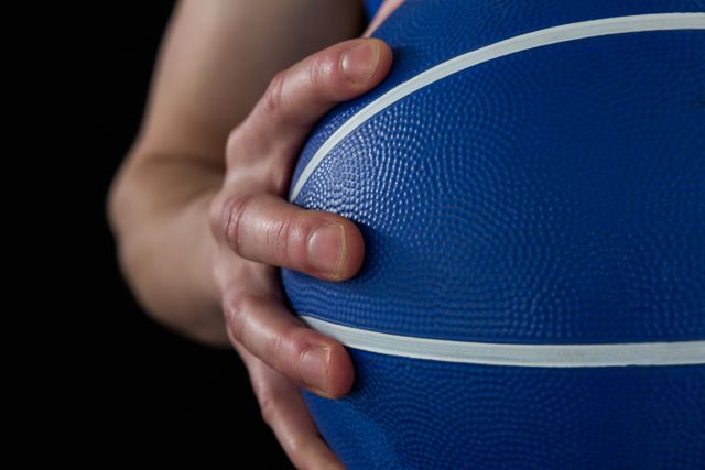 Mid section of player holding basketball against black background