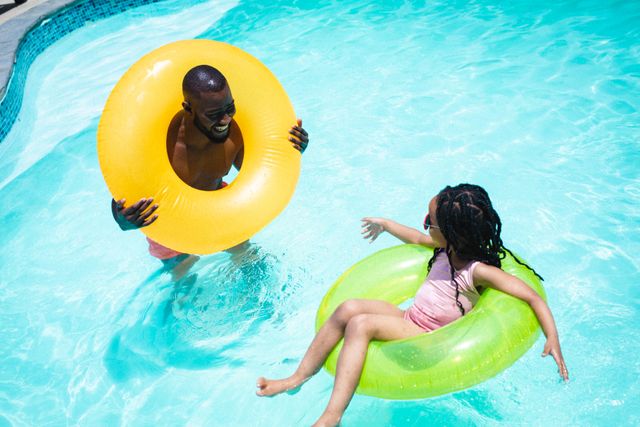 Happy african american father and daughter enjoying summer in swimming pool with inflatable rings - Download Free Stock Photos Pikwizard.com