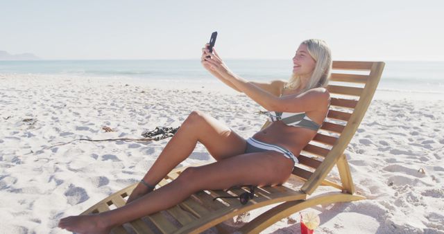 Happy caucasian woman sitting on deckchair and using smartphone on beach. Lifestyle, realxation, nature, communication, free time and vacation.