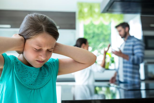 Sad girl covering her ears while parents arguing in background - Download Free Stock Photos Pikwizard.com