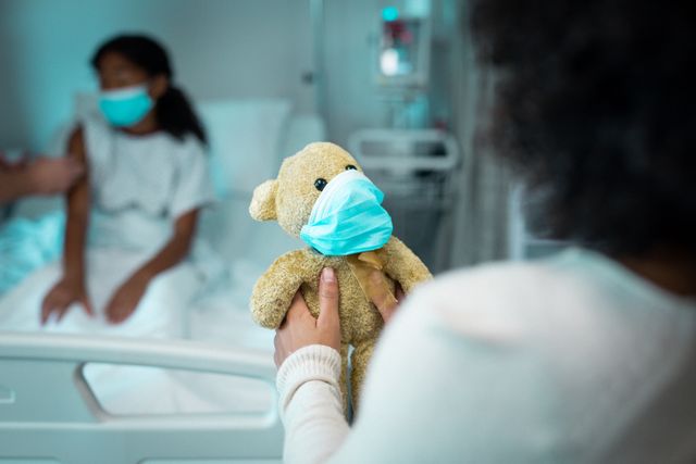 African american mother and daughter sitting on hospital bed, holding teddy bear, wearing face masks - Download Free Stock Photos Pikwizard.com