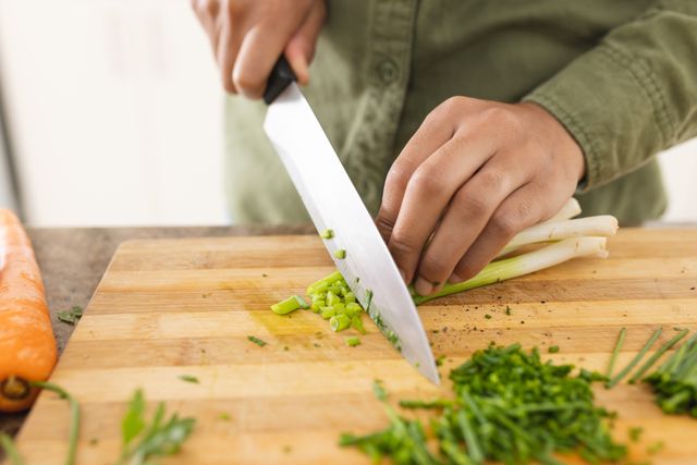 Close-up of woman chopping fresh scallions in kitchen at home. Unaltered, lifestyle, preparation, cooking, food, healthy, vegetable.
