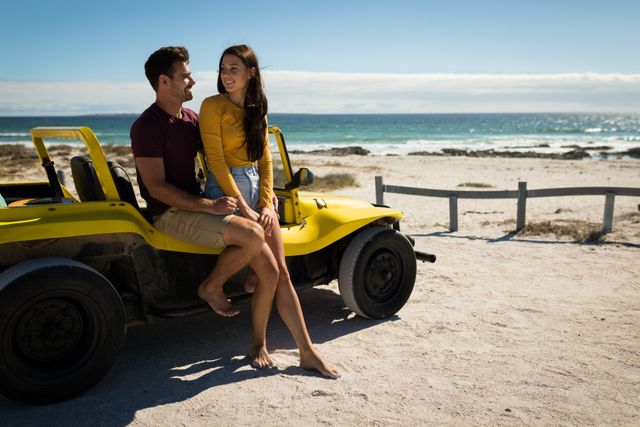 Happy caucasian couple sitting on beach buggy by the sea embracing and talking. beach stop off on romantic summer holiday road trip.