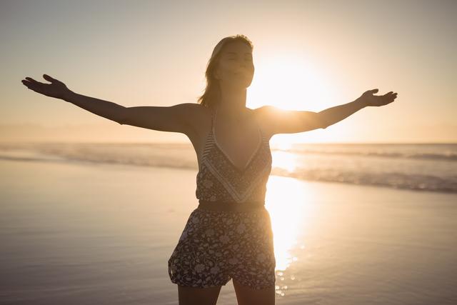 Young woman with arms outstretched standing at beach during dusk
