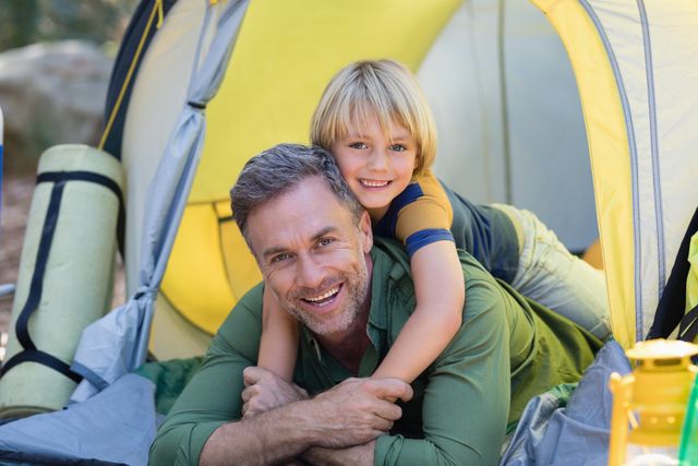 Little boy lying on father in tent at campsite - Download Free Stock Photos Pikwizard.com