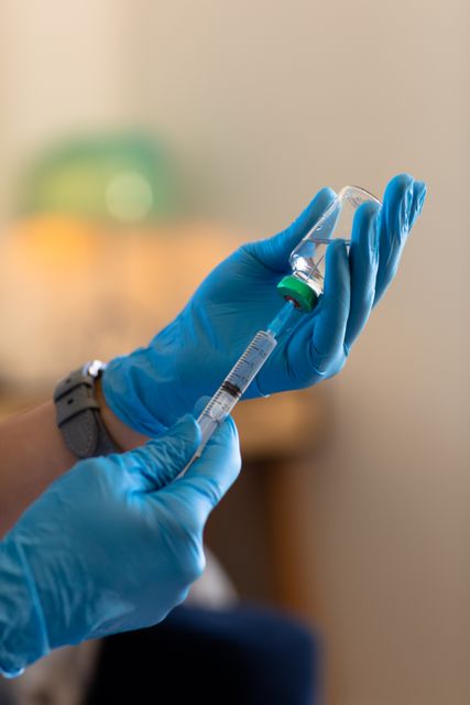 Cropped hands of caucasian doctor wearing gloves holding vial and syringe against white wall at home - Download Free Stock Photos Pikwizard.com