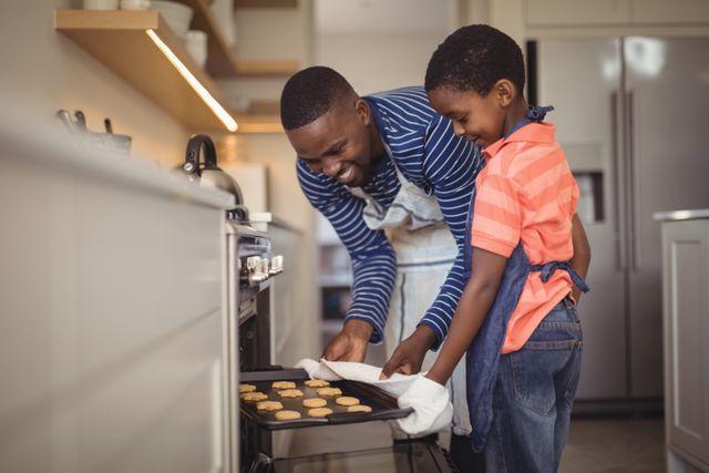 Father taking tray of fresh cookies out of oven with son in kitchen - Download Free Stock Photos Pikwizard.com