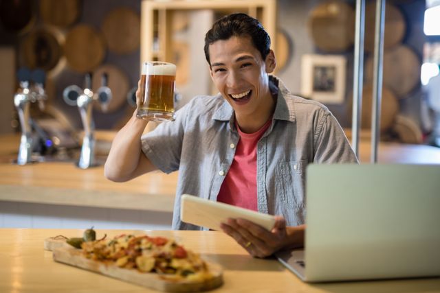 Smiling man holding beer mug and digital tablet in restaurant - Download Free Stock Photos Pikwizard.com