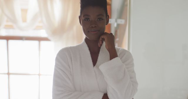 Portrait of african american attractive woman in white robe looking at camera and smiling. beauty, pampering, home spa and wellbeing concept.