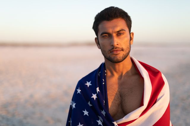 Portrait of man wrapped in American flag standing on the beach