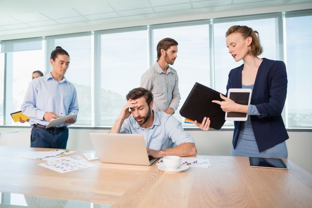 Colleagues with document, digital tablet and mobile phone talking to frustrated man in office
