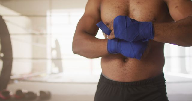 Image of midsection of fit african american man preparing for box training at gym. active, fit, sporty and healthy lifestyle, exercising at gym concept.