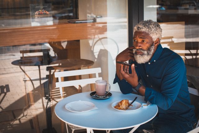 African american senior man sitting outside cafe having coffee and using smartphone - Download Free Stock Photos Pikwizard.com